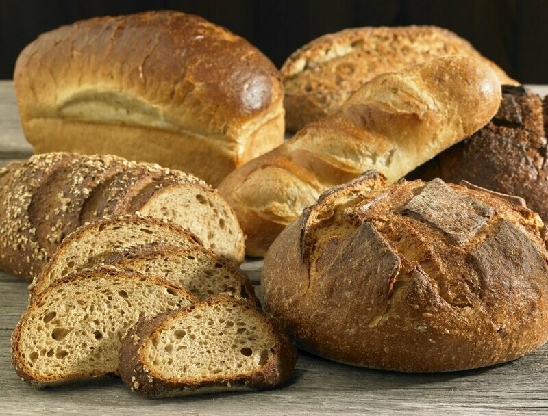 A wooden table of bloomers, baguette, seeded loaf and sourdough